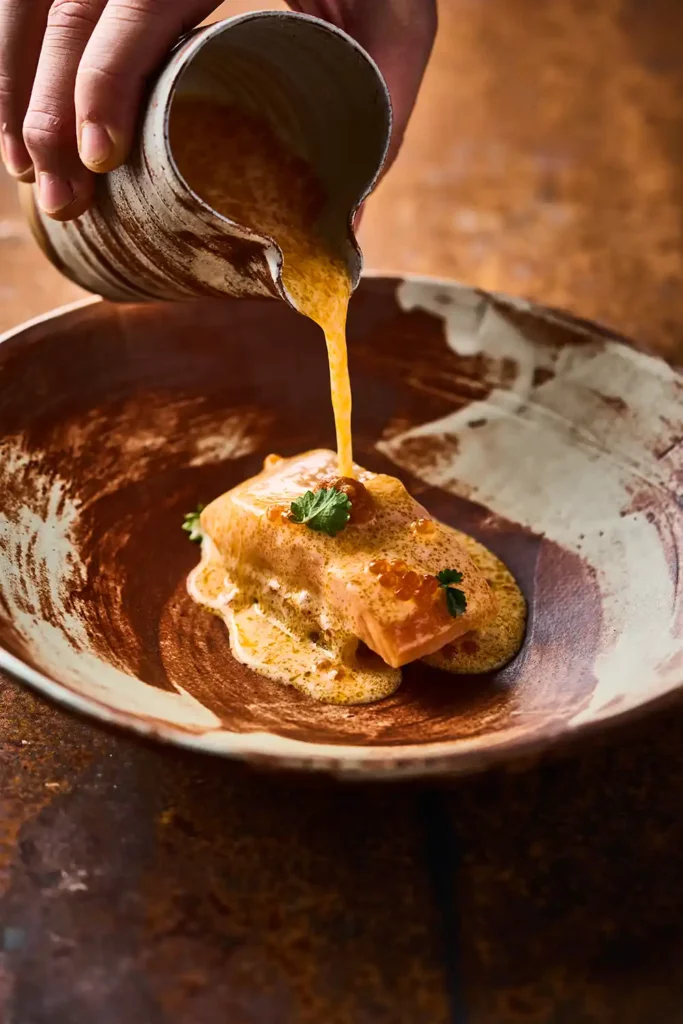 Sauce chaude versée sur un filet de poisson dans une assiette artisanale – photo culinaire raffinée à Lyon