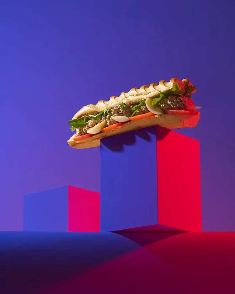 Sandwich thon, tomate, œuf et salade en lévitation sur des blocs violet et rouge — photographie culinaire artistique