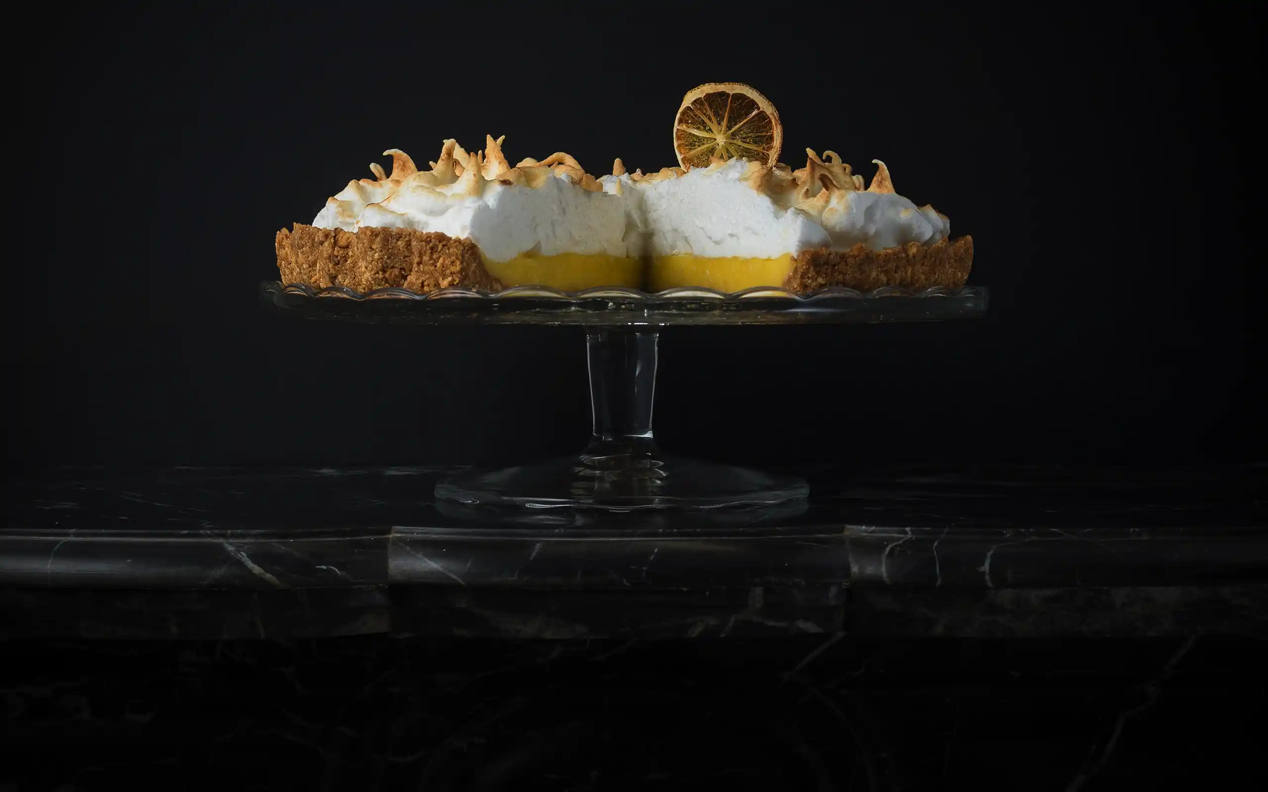 Tarte au citron meringuée sur présentoir en verre, fond noir clair-obscur — photographie culinaire Cherrystone à Lyon
