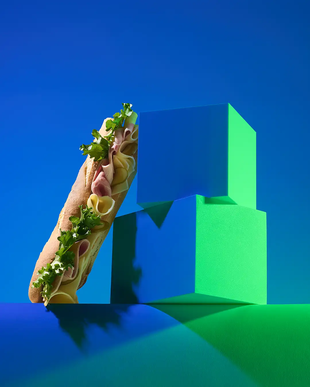 Sandwich jambon, fromage et roquette photographié sur fond bleu et vert, prise de vue de produit en studio.