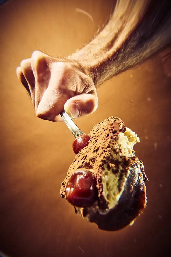 Cuillère de dessert crémeux au cacao et cerises amarena tendue vers l'objectif sur fond ocre — série culinaire « Mange ! », photographe culinaire à Lyon.