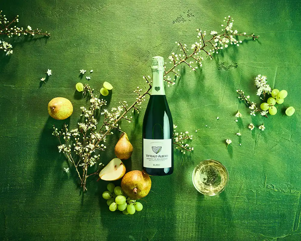 Planche d'ambiance crémant de Bourgogne Blanc Vitteaut-Alberti, poires, raisins blancs et fleurs de prunellier sur fond vert