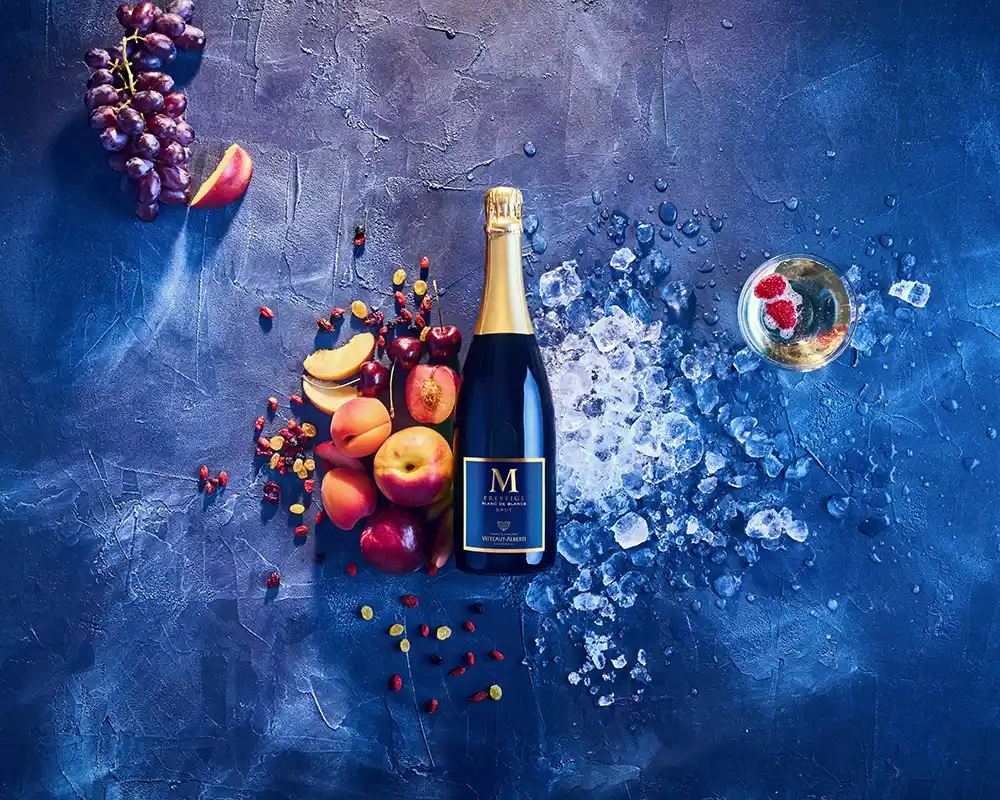 Planche d'ambiance crémant de Bourgogne M Prestige Vitteaut-Alberti, fruits rouges, abricots et glace pilée sur fond bleu nuit