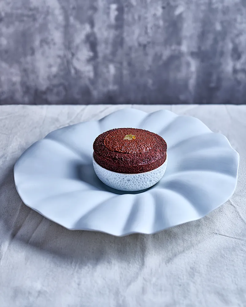 Soufflé au chocolat du chef Benoît Charvet sur assiette pétale, fond béton, photographie culinaire éditions Bocuse, photographe Lyon