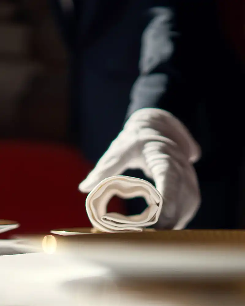 Détail en clair-obscur d'une main gantée de blanc pliant une serviette, arts de la table, restaurant Saisons, photographe culinaire Lyon