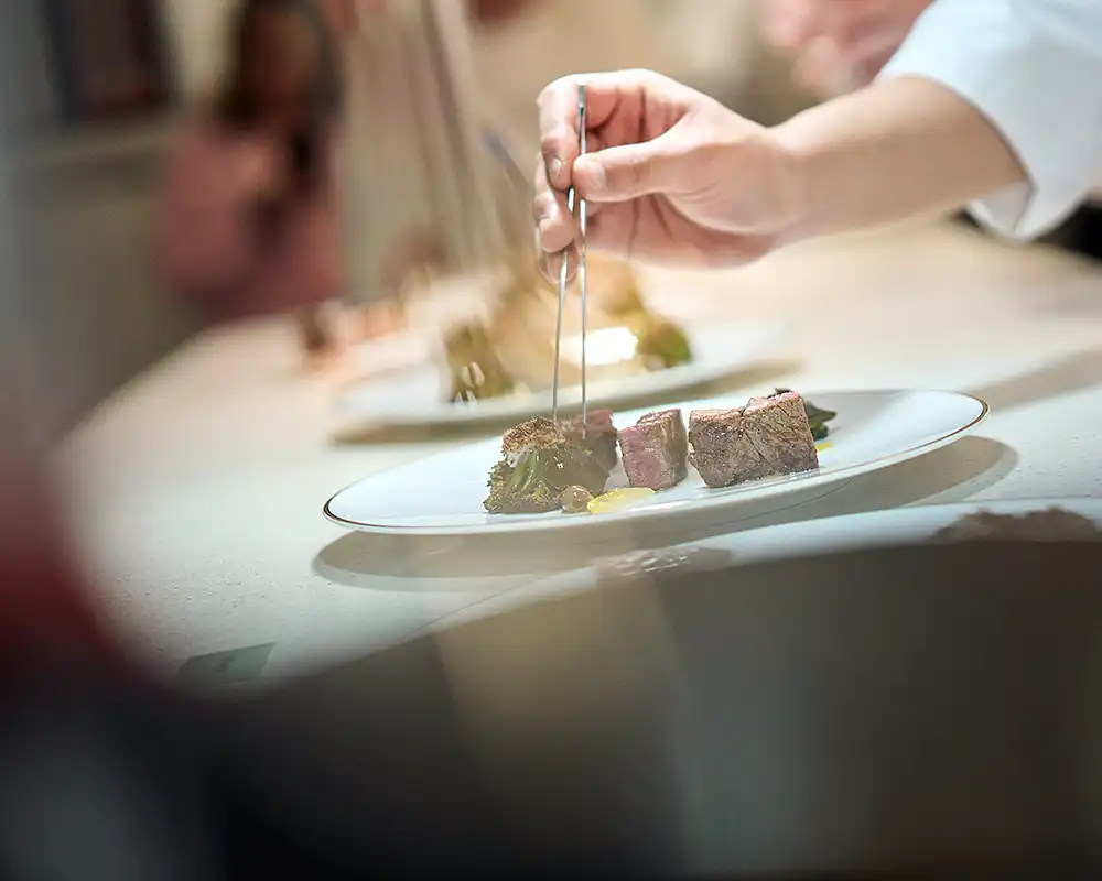 Dressage à la pince d'un plat de viande en cuisine, profondeur de champ courte, restaurant Saisons, photographe culinaire Lyon