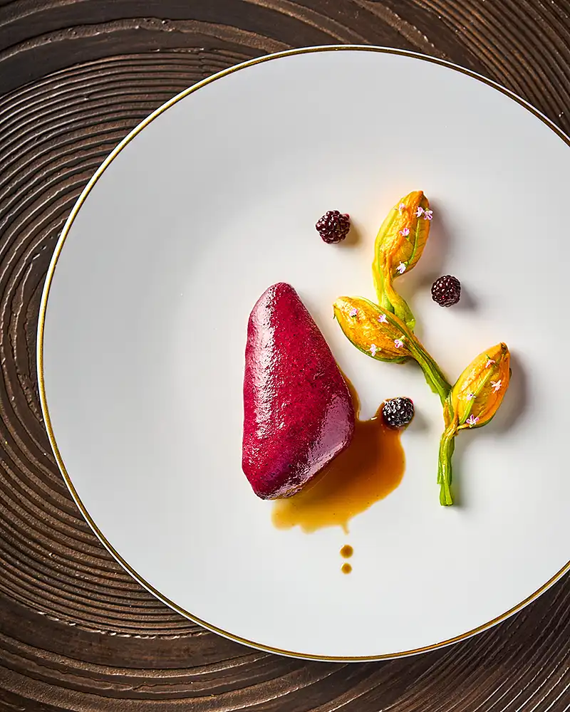 Plat gastronomique quenelle de betterave, fleurs de courgette et mûres sur assiette à filet or, vue de dessus, restaurant Saisons, photographe culinaire Lyon