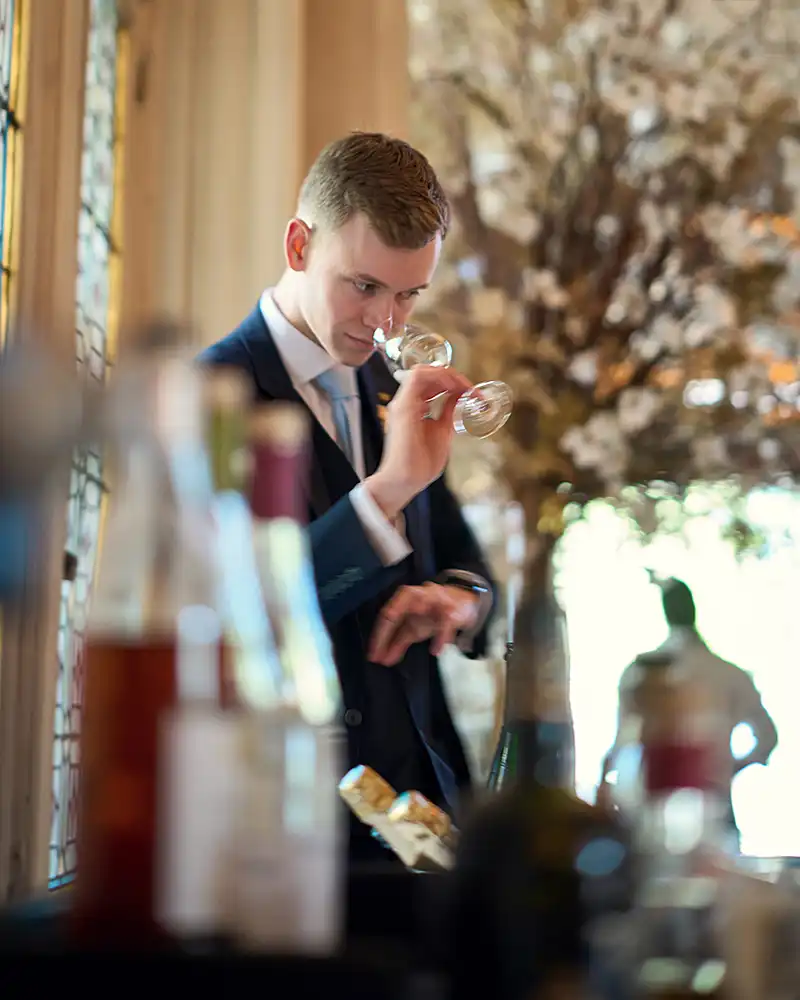 Sommelier au nez du verre en dégustation, bokeh de bouteilles au premier plan, restaurant Saisons, photographe culinaire Lyon