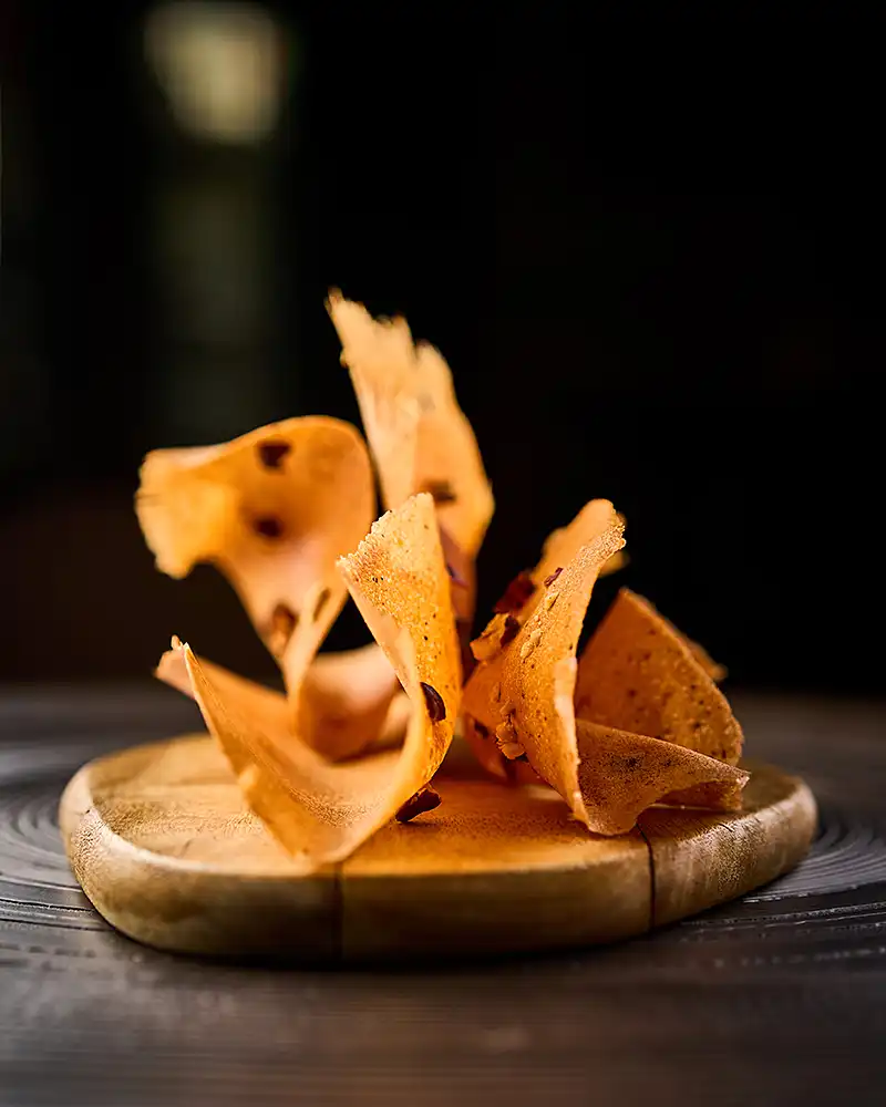 Tuiles croustillantes dressées en volume sur une planche de bois, fond sombre, lumière dure, restaurant Saisons, photographe culinaire Lyon